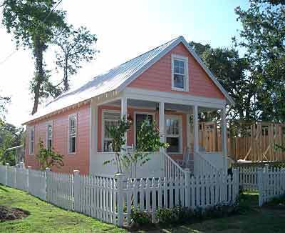 A very small pink house is surrounded by a white picket fence.