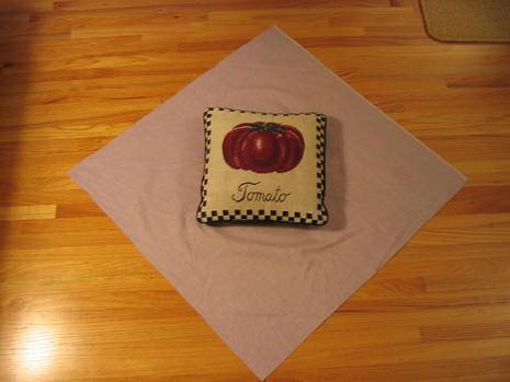 A small pillow with a tomato is on a pink napkin.