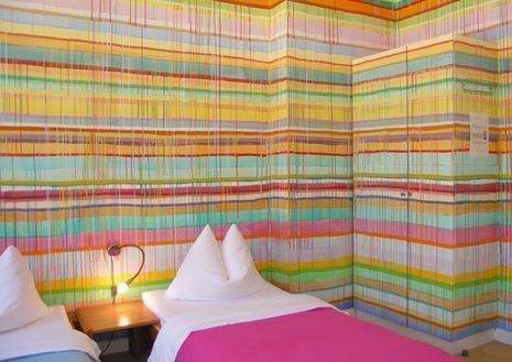 A pink and a light blue bed are in a colorful room with striped walls.