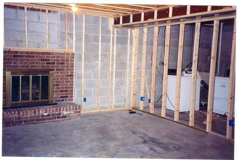 A basement divided by a wall frame with a fireplace on one side and laundry appliances on the other.