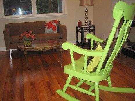 A green rocking chair sits in a room with wooden flooring.