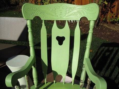 A chair made out of wood is green and sitting outside.