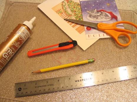A placemat where several craft supplies lay, such as a ruler, glue, a pencil, a knife, a pair of scissors, and some greeting cards.