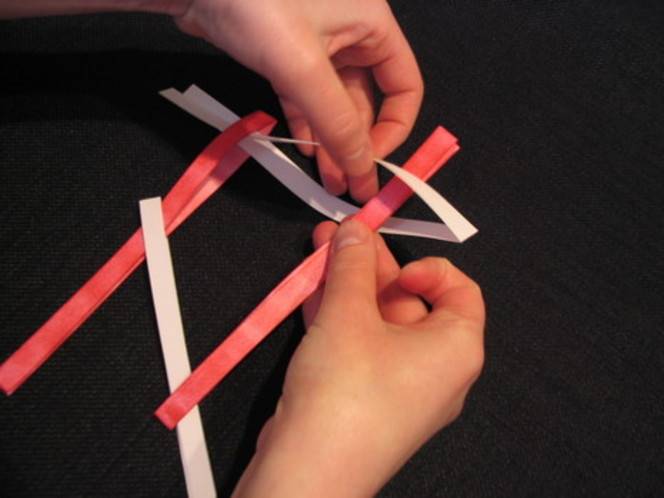 Strips of folded red and white paper are glued and fastened together to create an art piece.