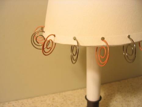 A small white lampshade with different color metal spirals hanging from holes around its rim.