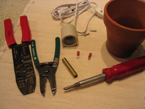 An assortment of tools—including a a cutting tool and a screwdriver—on a wooden surface along with a roll of tape, an extension cord and a garden pot.