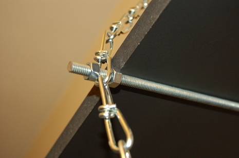 Metal chain attached to a screw on a rod that is attached to a wooden board.