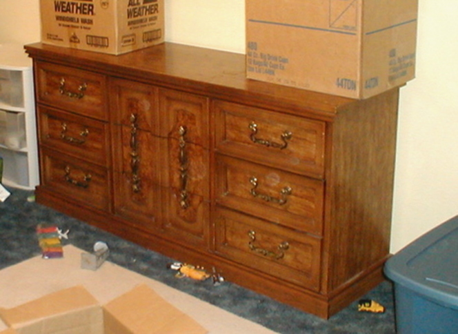 A brown dresser little toys scattered at the base and with two carboard boxes on it.