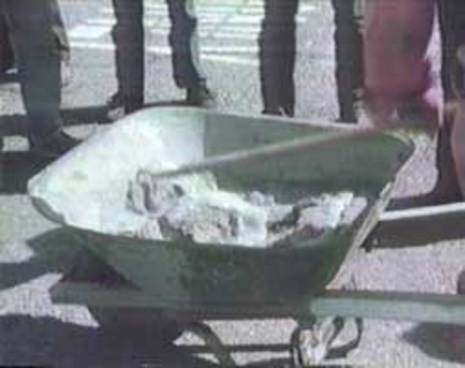 A wheelbarrow half full of wet cement with a mixing hoe inside of it.