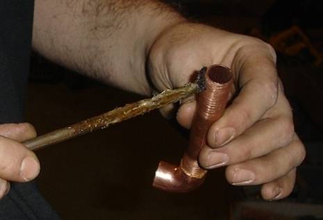 A man holding a copper pipe applying a lube to the thread.