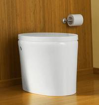 A white bathroom trashcan sits against a wooden floor and wall, while a toilet paper dispenser is attached to the wall.