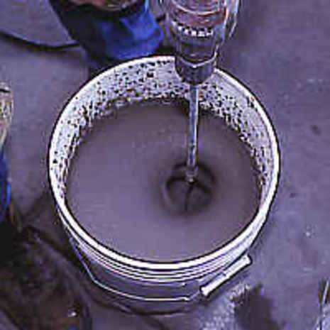 Person mixing a batch of concrete with mixer in bucket.