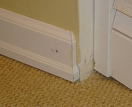 A white baseboard against a yellow wall is showing a problem.