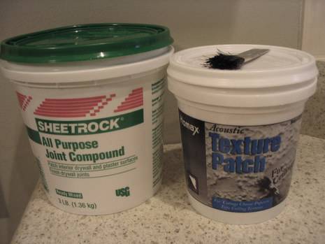 Container of sheetrock joint compound sitting beside a container of texture patch with a brush on the lid.