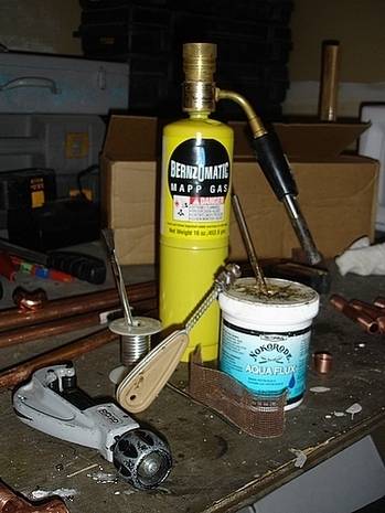 A gas tank, copper wires, a vise grip, and a few assorted things laying on a work bench.