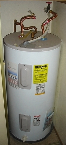 Round white water heater with brass pipes sprouting from the top.