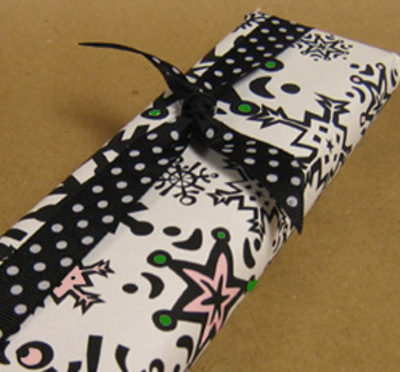 A long box that has been fgift wrapped with white paper and pink and green accents with a black and white polka dot bow.