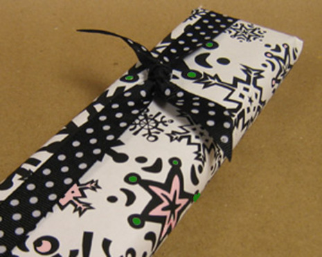 A long box that has been fgift wrapped with white paper and pink and green accents with a black and white polka dot bow.