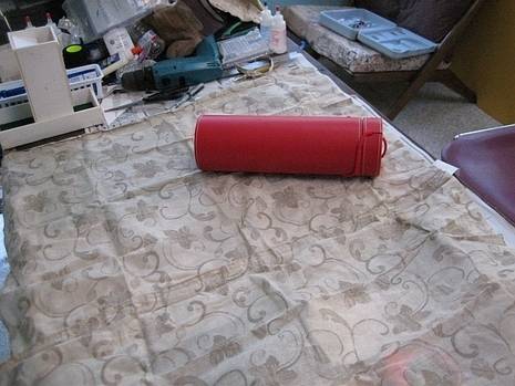 A red thermos holder on top of a piece of fabric next to a bunch of junk.
