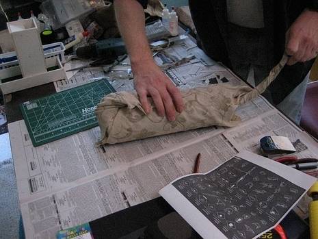 A persons hand wrapping a cylindrical item on a table on top of newspaper.