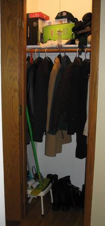 Dark colored clothing hang in a closet.