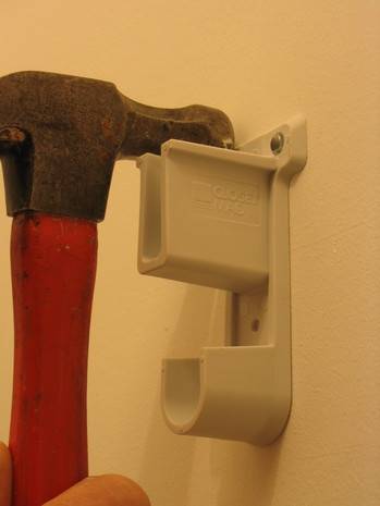 A hammer finishing up putting in a small plastic hook of sorts into the wall.