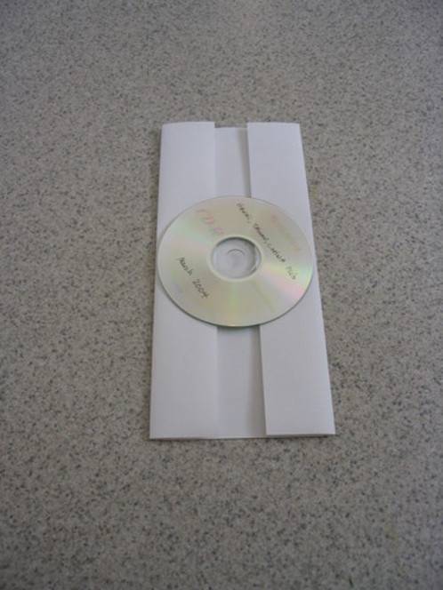 A compact disc rests on a piece of paper whose sides are folded lengthwise.