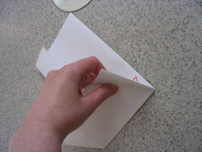 A chubby pink hand holding a folded white paper over a mottled table.