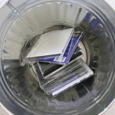 A pile of CDs discraded in a metal trash can.