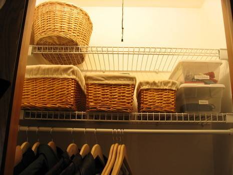 Wicker baskets sit on a closet shelf above a row of hangers.