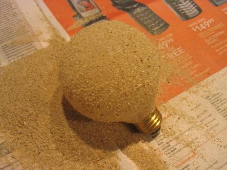 A round light bulb, coated with sand, on a piece of newspaper.