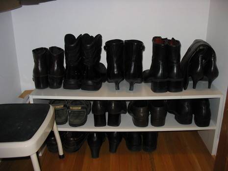 A shoe rack consisting of two shelves that hold several pairs of black boots and shoes next to a step stool.
