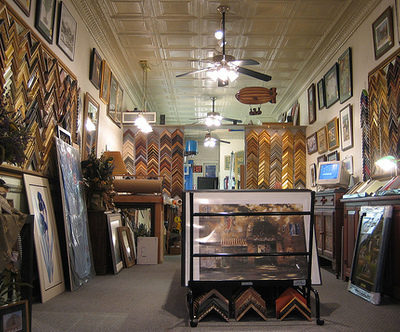 A frame store with ceiling fans in the middle and loads of frames on either wall.
