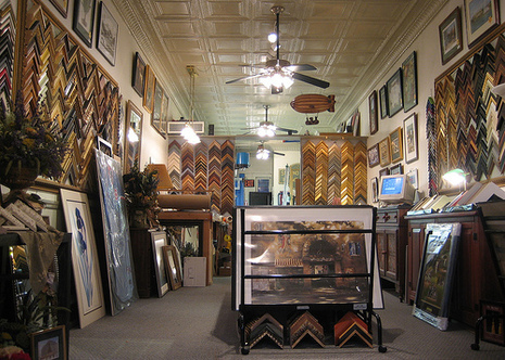 A frame store with ceiling fans in the middle and loads of frames on either wall.
