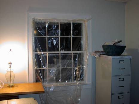 Plastic sheeting is covering a window in a white room.