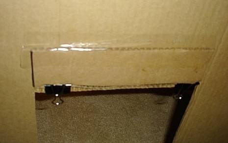 A large piece of cardboard with a door cut out has two large clips at the top of the opening.