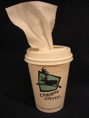 A cup with Caribou coffee on it has a tissue hanging out of the top.