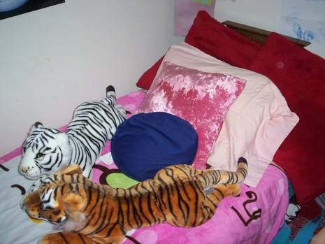 Two stuffed tigers are sitting on a bed with pillows.