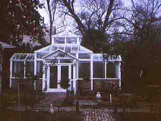 Exterior view of a large house shaped greenhouse with clear windows and white trim.