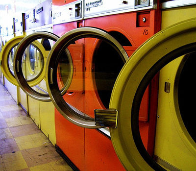 A row of washing machines, some orange, some yellow, in a laundromat with their doors open.