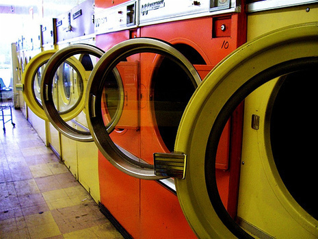 A row of washing machines, some orange, some yellow, in a laundromat with their doors open.