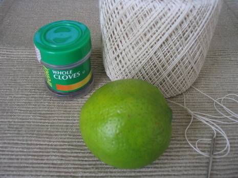 A spool of white string next to a bottle of whole cloves and a lime.