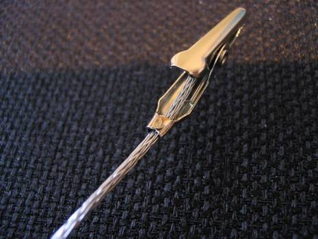 A small brass colored roach clip attached to a thin metal cord.