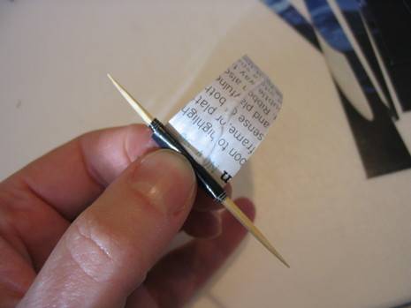 A finger and thumb holding a toothpick with a small piece of paper wound around it.