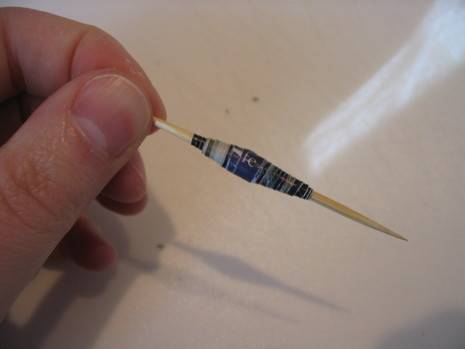 A man holds a toothpick with some sort of thin plastic wound around it to create a bobbin like look.