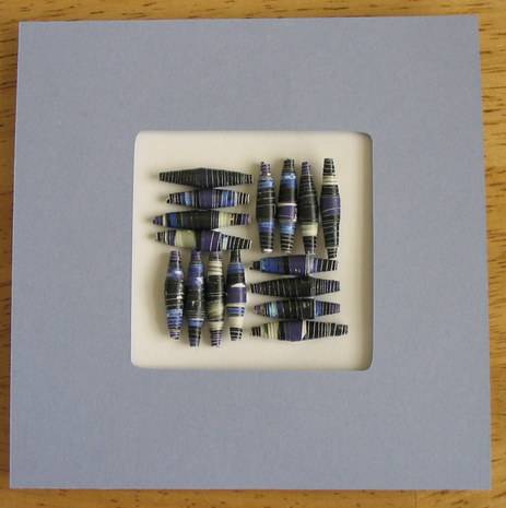 A square matted piece of art using beads to form a design in the center.