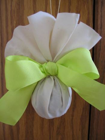 A pomander housed in white muslin fabric and held together with a light green bow.