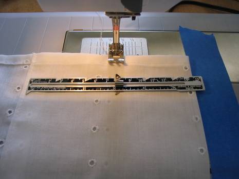 White eyelet fabric is being sewn on a sewing machine with white painter's tape on it.