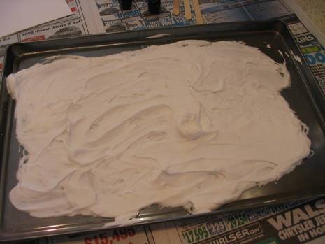 Frosting somewhat evenly spread out on a rectangular cookie sheet.