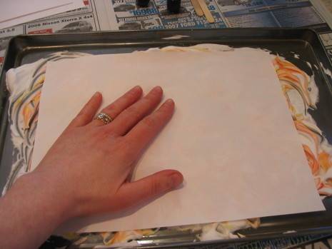 A person holds a white piece of paper on paint on a tray.